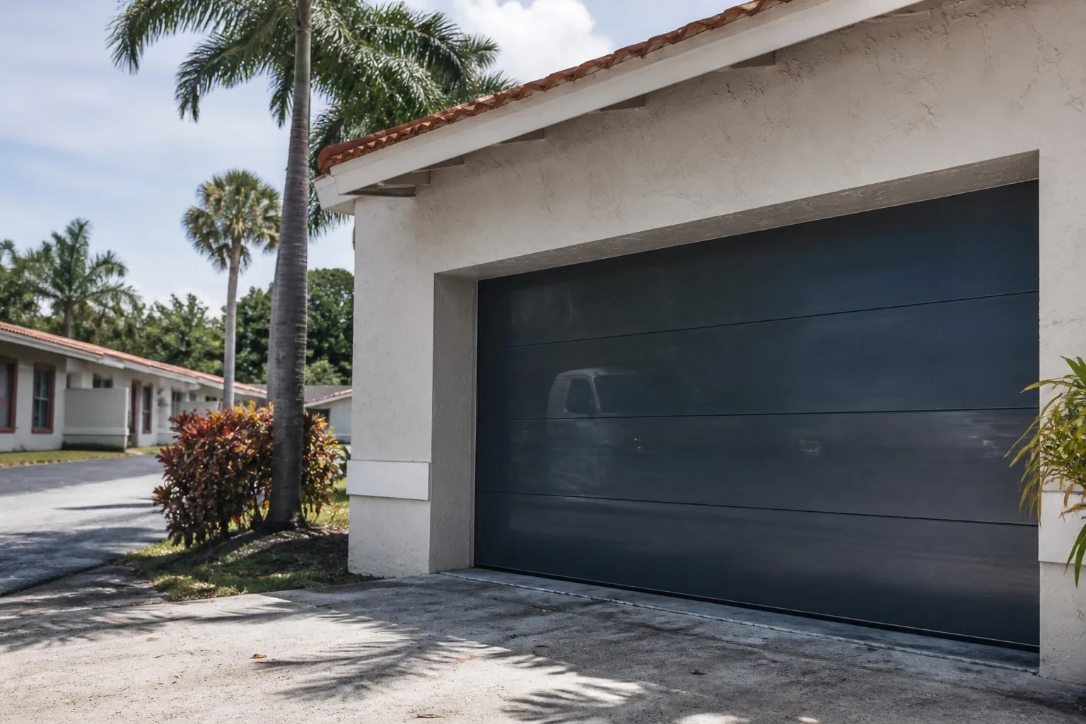 Dark sectional garage door set into a white stucco home beside a palm tree